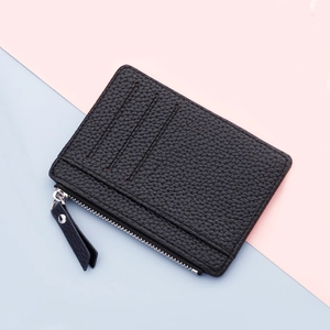 Slim black leather card holder with three card slots and zipper pocket on dual color background