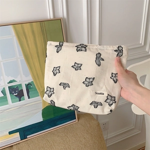 Detalle de la bolsa de maquillaje en lona crema con motivos florales y etiqueta tejida