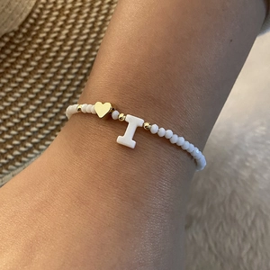 Macro detail of white beaded bracelet with gold heart and letter I charm on model