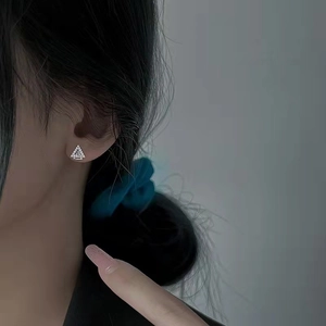 Macro shot of silver geometric triangle stud earrings with micro-set zircon on ear