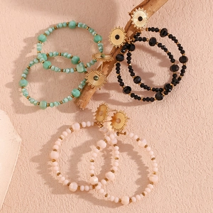 Detail of bohemian beaded hoop earrings in mint, black, and white on natural wood branch