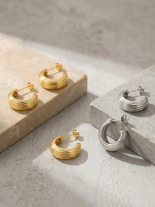 Détail des boucles d'oreilles rayées en forme de C en finitions or et argent sur marbre