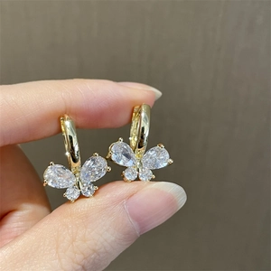Macro shot of sparkling zircon butterfly earrings with gold plating on a finger