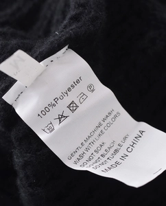 Close-up of the wash care label on a black knit cardigan showing size and 100% polyester
