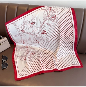 Close-up of silk scarf with red lily pattern and geometric stripes on leather sofa