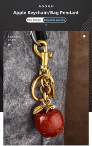 Macro view of a sparkling red apple keychain with golden leaf on a textured bag