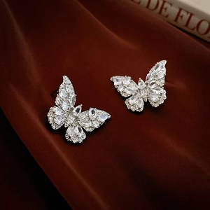 Macro shot of silver butterfly stud earrings with clear zircon on red silk background