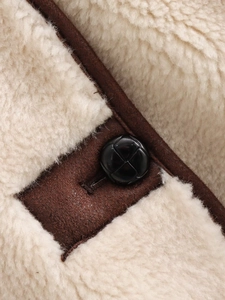 Macro detail of faux shearling texture with contrast trim and woven leather button closure