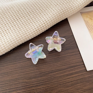 Macro shot of two star-shaped iridescent acrylic hair clips on a dark wood background