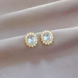 Detailed close-up of gold oval stud earrings with clear zircon stones on grey silk fabric