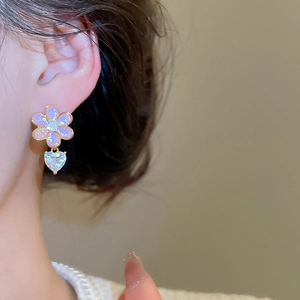 Detail view of purple resin flower earrings with heart-shaped zircon pendants on a model