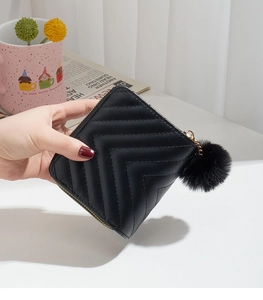 Close-up of black V-quilted short wallet with gold zipper and decorative pompom charm