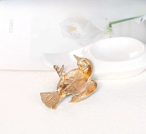 Detail view of the gold bird brooch back featuring secure safety pin and alloy texture