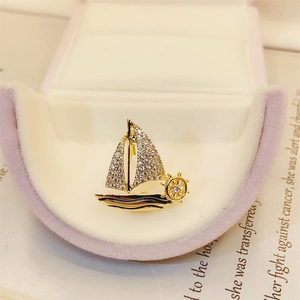 Detailed close-up of a golden sailing boat brooch with crystal rhinestones on a velvet box