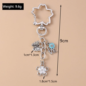 Macro detail of silver keychain with butterfly, blue love charm and white flower pendant