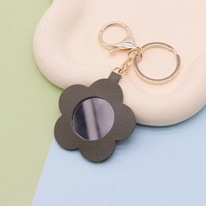 Detail of flower shaped green faux leather keychain with a small circular mirror and gold clasp