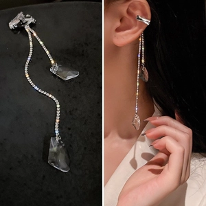 Détail d'un ear cuff argenté à pompon long avec strass et pendentifs sur un modèle