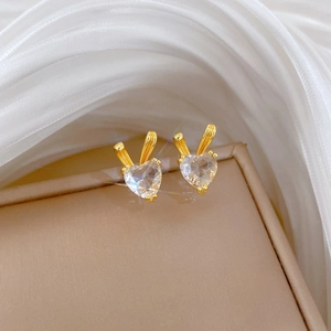 Detail of gold rabbit ear earrings with heart-shaped crystals on beige jewelry box