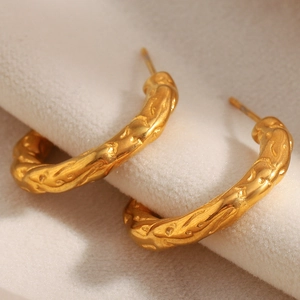 Macro view of gold-plated irregular textured hoop earrings on soft beige velvet fabric