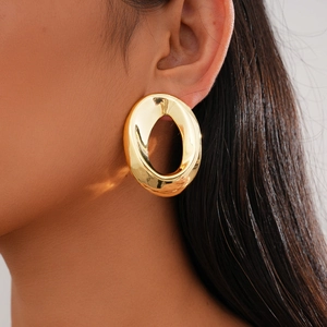 Close-up of a large gold irregular oval earring with a polished mirror finish on model