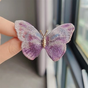 Macro shot of embroidered butterfly brooch with purple gradient wings and gold metal body