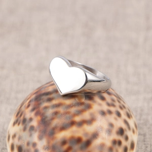 Polished silver heart signet ring in stainless steel displayed on a natural sea shell