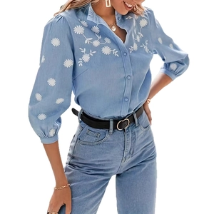 Dettaglio del ricamo di margherite bianche su camicia in denim blu chiaro