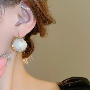 Détail de boucles d'oreilles perles baroques avec bord doré sur l'oreille du mannequin