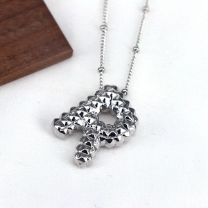 Macro detail of silver letter R pendant necklace with unique studded 3D rivet texture