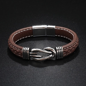 Macro detail of brown braided leather bracelet with silver knot metal buckle on black background