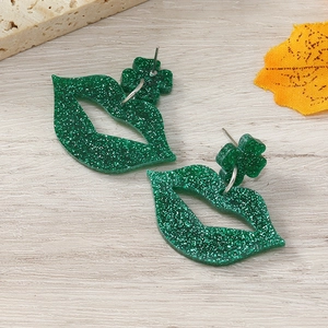 Detail von grünen Glitzer-Lippen und Kleeblatt-Ohrringen auf einem Holzgrund