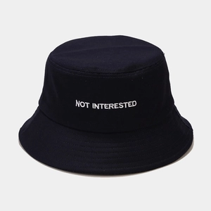 Primo piano dettagliato del ricamo bianco NOT INTERESTED su un cappello a secchiello nero