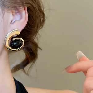 Close-up of golden C-shaped earring with black oval stone on model's ear