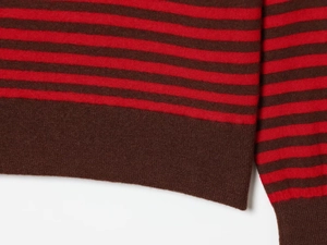 Détail d'un pull en maille rayé rouge et marron montrant la texture et l'ourlet