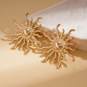Detail of golden sunray earrings leaning on white textured stone with warm lighting