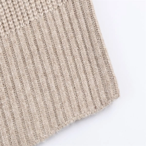 Détail macro des poignets en maille côtelée fine sur un pull beige à manches longues