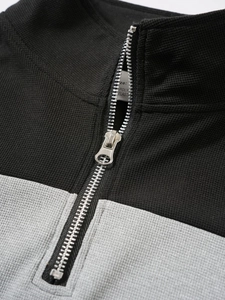 Gros plan sur la fermeture éclair et la texture gaufrée de ce polo gris et noir vintage