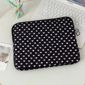 Detailed top view of a black quilted laptop sleeve with heart patterns on a desk