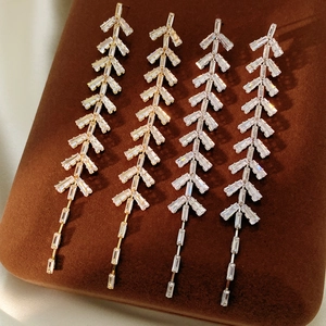 Macro shot of leaf-shaped tassel earrings featuring zircon inlay and golden finish details