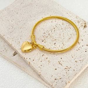 Golden heart pendant bracelet with twisted cable texture on elegant stone pedestal
