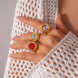 Detail of three stackable gold rings featuring large square pink, clear, and red zircons