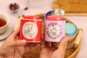 Close-up of red and purple tinplate tea canisters with Alice-style wedding illustrations