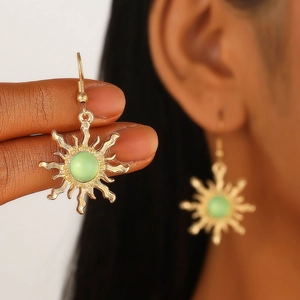 Close-up of golden sunburst drop earring featuring a central green gemstone detail