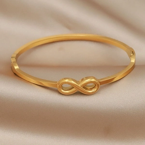 Minimalist gold infinity knot stainless steel bangle bracelet on champagne silk fabric