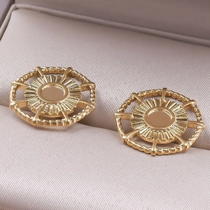 Macro view of gold stainless steel sunburst stud earrings on a beige jewelry cushion