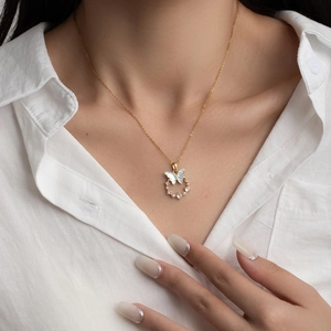 Detail of a gold butterfly necklace with pearl and zircon worn on a white shirt