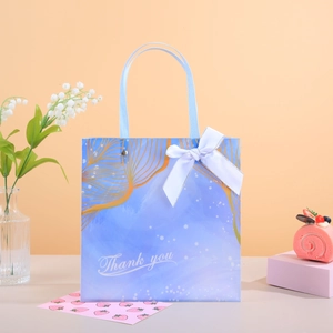 Détail du sac cadeau bleu clair avec motif de feuilles dorées, texte et nœud bleu