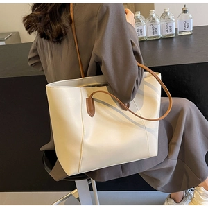 Detail of minimalist cream tote bag with brown straps styled on a grey blazer suit