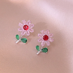 Macro shot of pink heart flower earrings with zircons and green leaves on silk