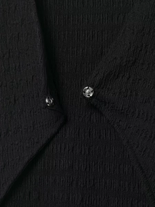 Gros plan sur la texture du tissu noir et deux boutons-pression métalliques sur la robe